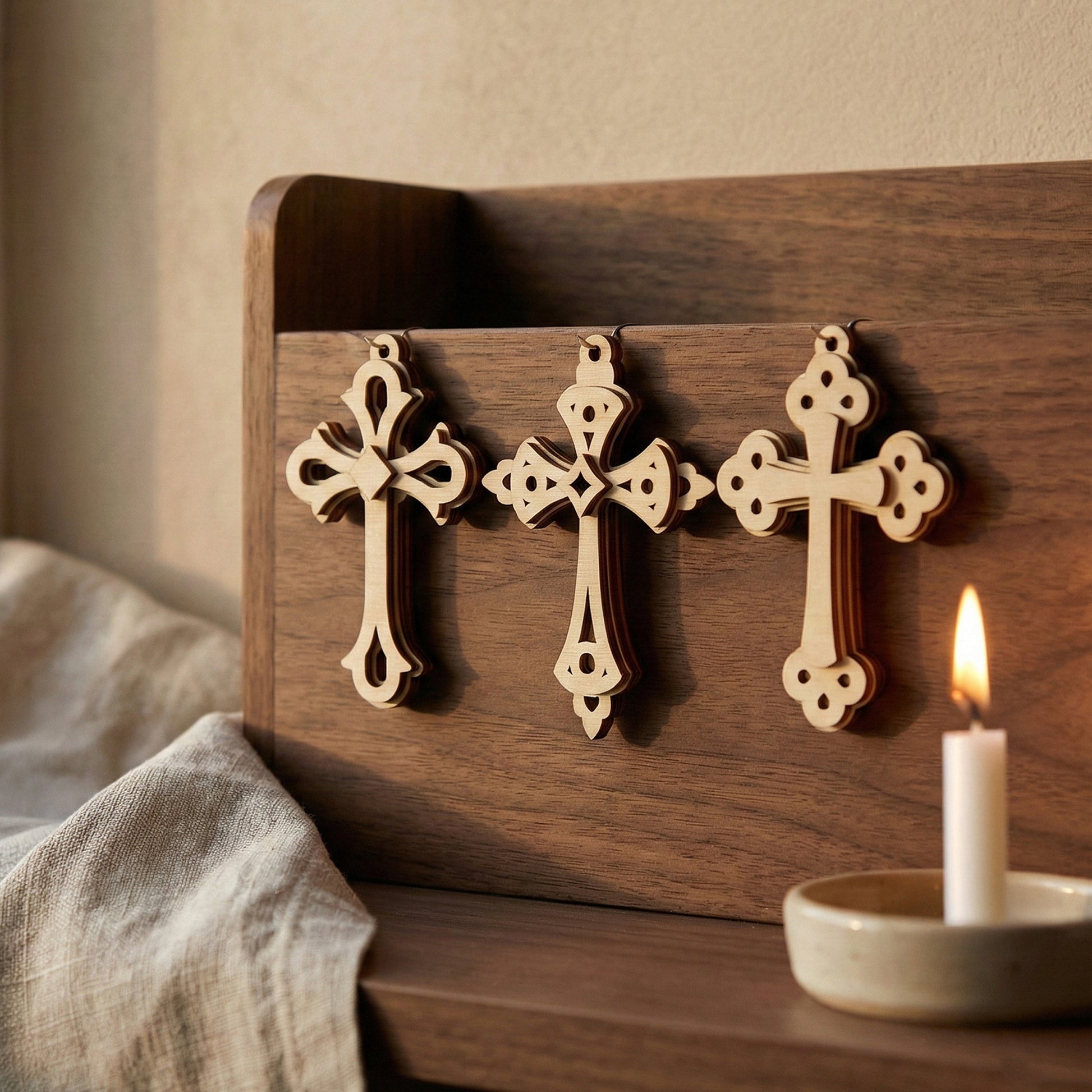 Wooden laser cut cross decorations on a wooden board with a lit candle in the background.