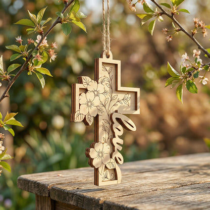 Wooden laser cut cross with floral designs and 'love' engraved, hanging outdoors on a branch.