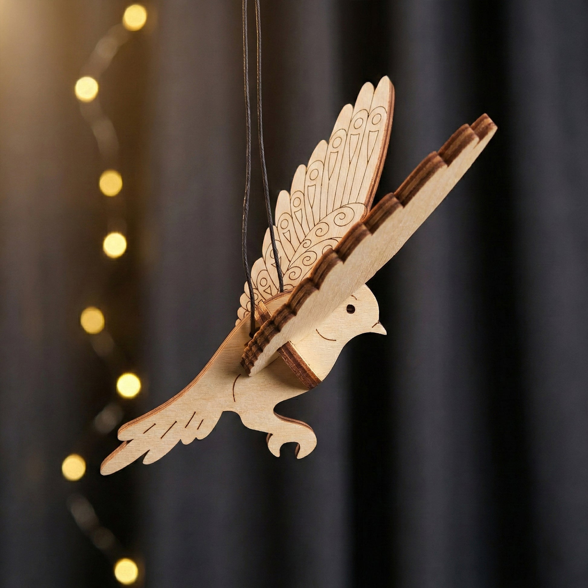 Wooden laser cut dove ornament hanging against a dark background with blurred lights