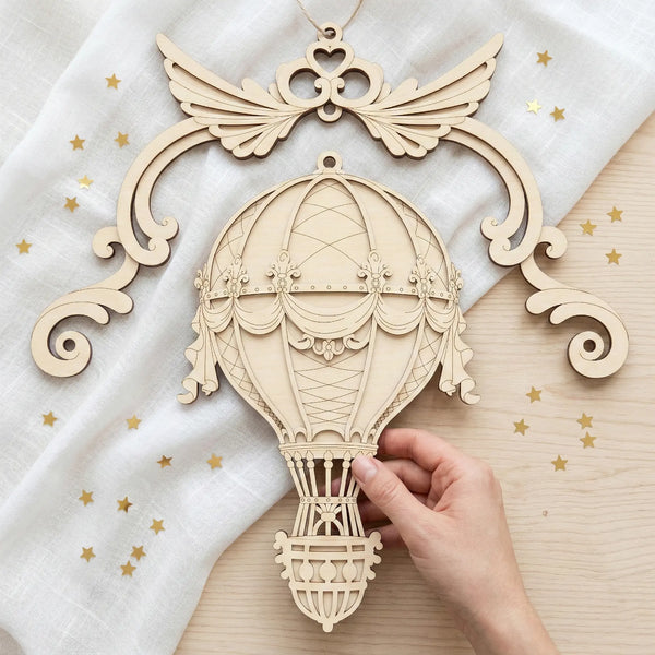 Laser cut hot air balloon airship ornament with decorative wings held by a hand on a light background.