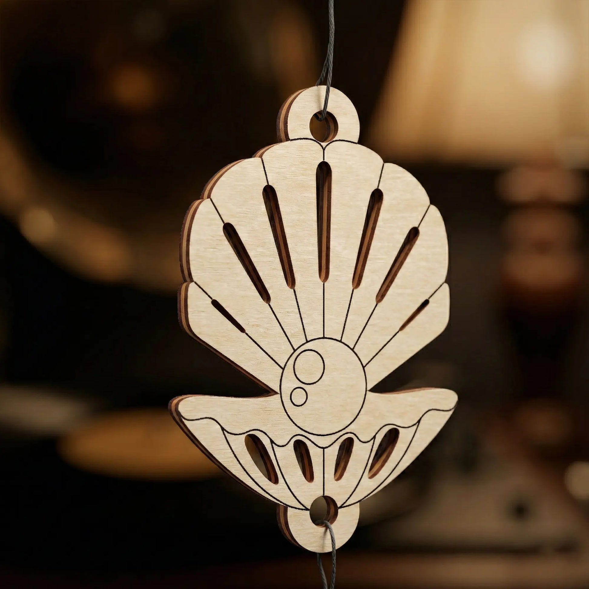 Wooden shell-shaped laser cutornament hanging against a blurred background