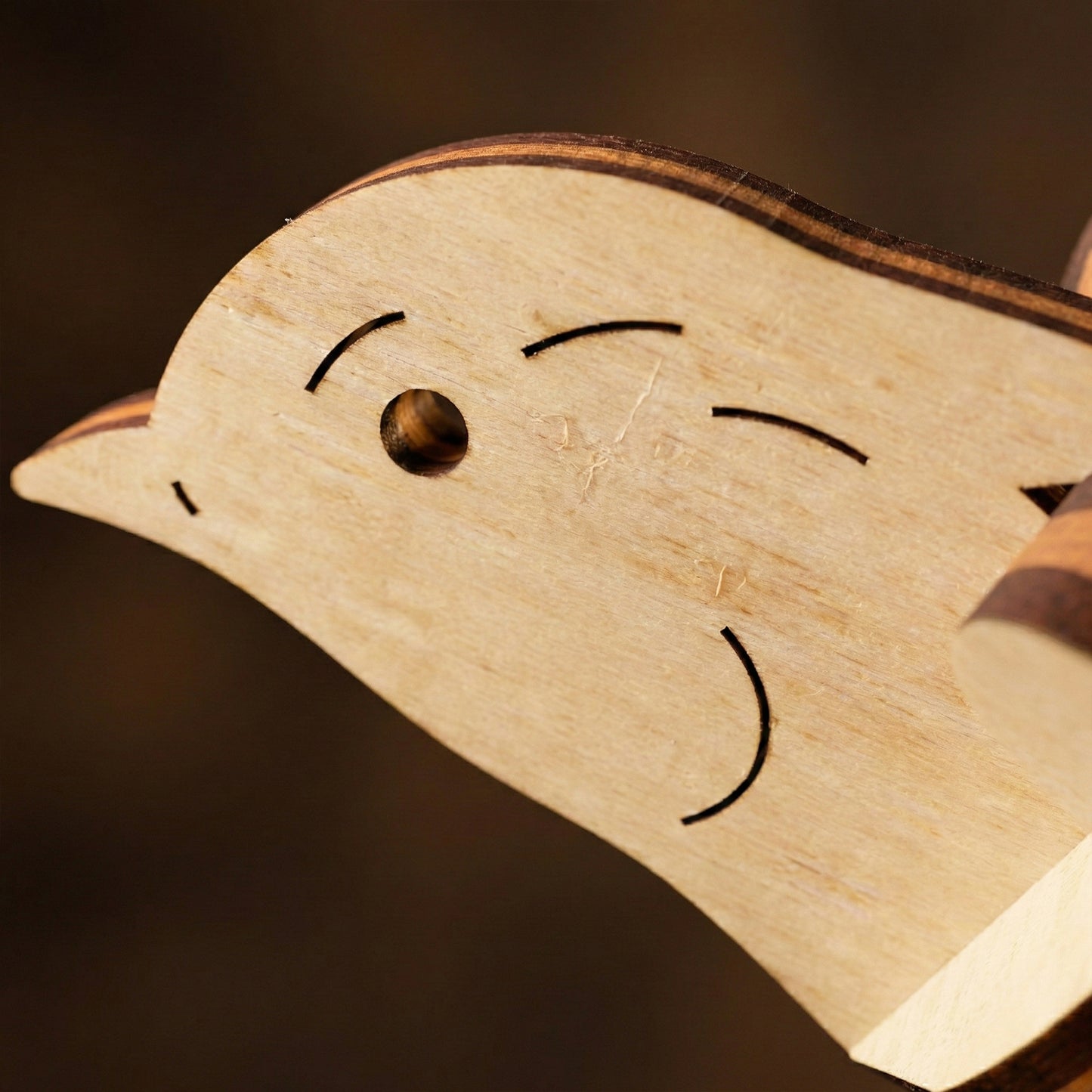 Wooden laser cut duck-shaped object with a face drawn on it against a dark background