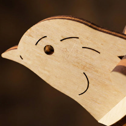 Wooden laser cut duck-shaped object with a face drawn on it against a dark background