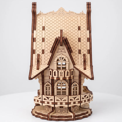 A 3D wooden model of an ornate Victorian-style house, constructed from laser-cut light brown wood with darker brown engraved details, shown on a light gray background.
