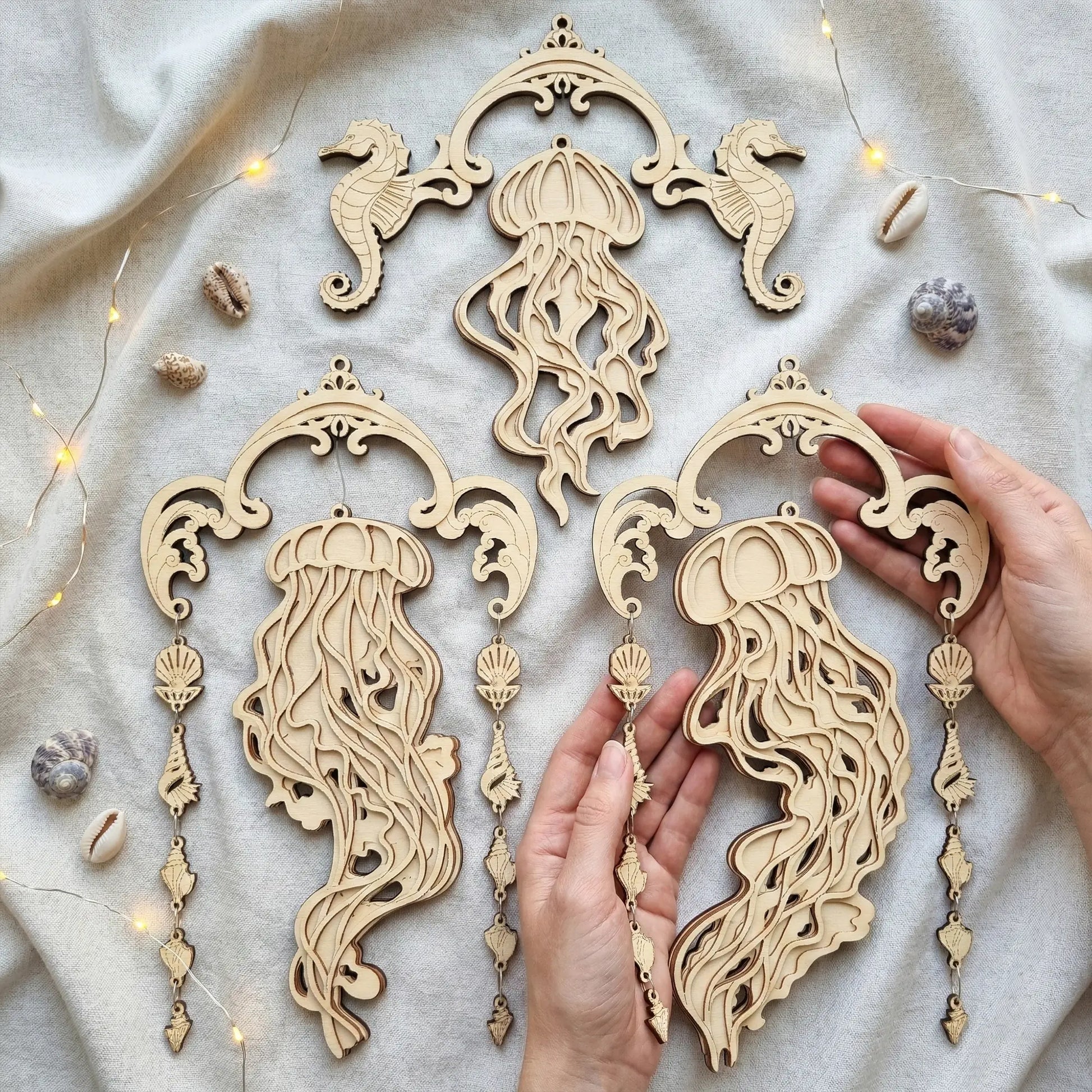 Wooden jellyfish and seahorse laser cyt decorations on a neutral fabric background with hands holding one of the decorations.