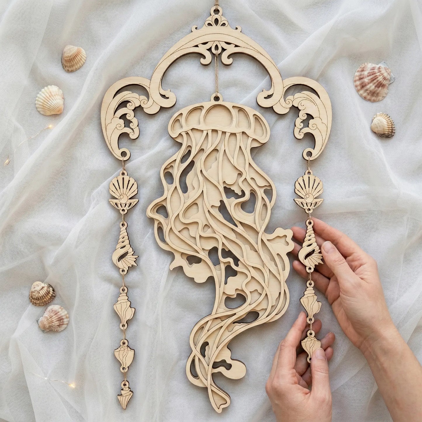 Laser cut jellyfish wall decor with hand holding it on a light fabric background