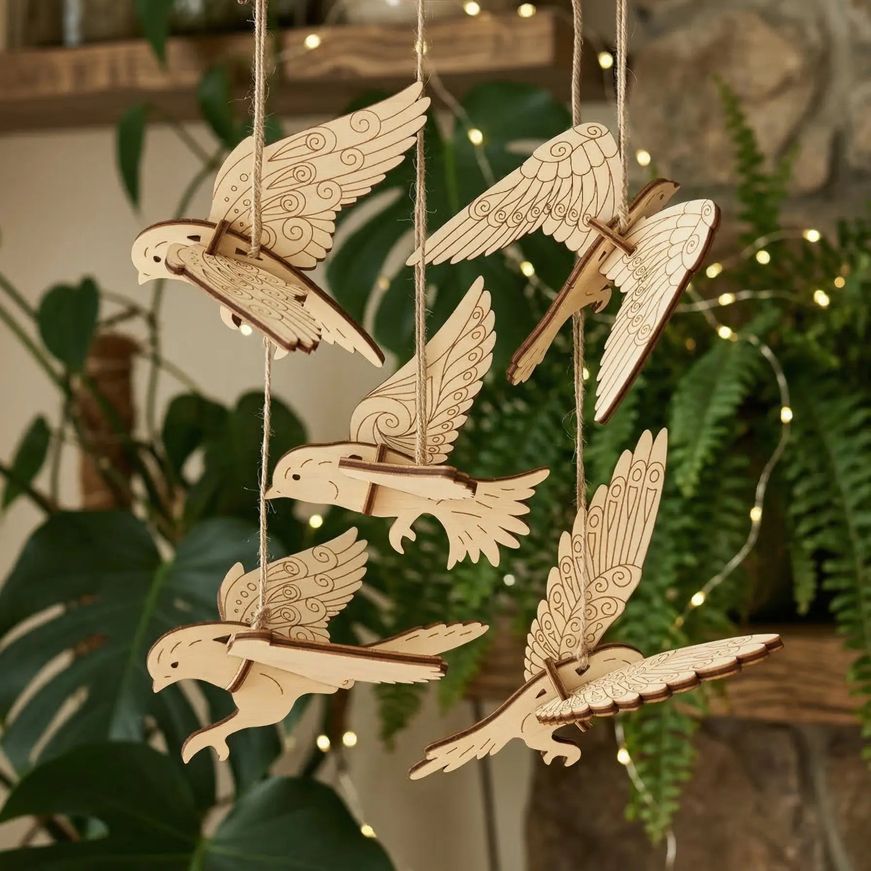 Wooden laser cut bird decorations hanging against a natural background with plants and lights.