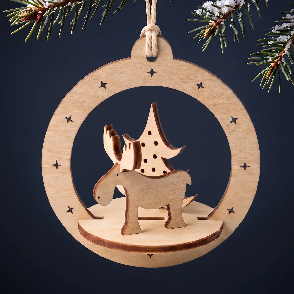 Laser cut plywood deer bauble ornament hanging from snow-dusted fir tree bough against dark holiday background.