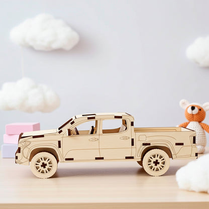 Laser cut plywood wooden 3D model kit of a pickup truck with four doors and an open bed, showcased on a light wooden surface in a nursery room with cloud decorations on a blue wall, toy blocks, and a knitted animal