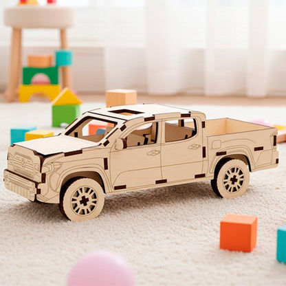 Laser cut plywood wooden 3D model kit of a modern pickup truck with four doors and an open bed, displayed on a soft white rug surrounded by colorful toy blocks in a bright indoor playroom setting