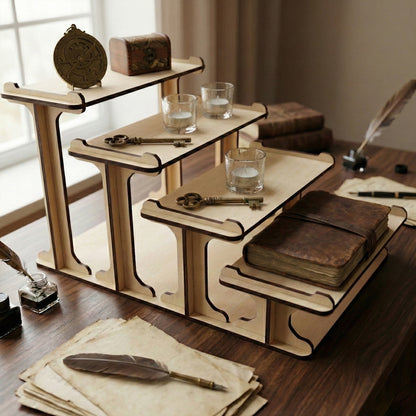 Laser cut 4-tier wooden plywood shelf displaying vintage items: antique keys, leather-bound journals, glass candles, and an astrolabe. Dark wood desk setting with an inkwell and quill, showing the stand's versatility for aesthetic home office decor