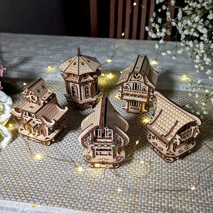 Top view of five diverse laser cut plywood village houses arranged together on a tablecloth with festive light string.