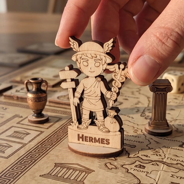 Adult hand placing a laser cut plywood Hermes figurine on a detailed board game map with Greek patterns and game tokens