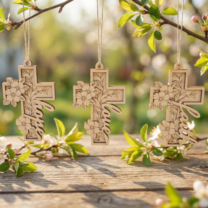 Three wooden laser cut cross ornaments with floral designs hanging on a branch with leaves and flowers.