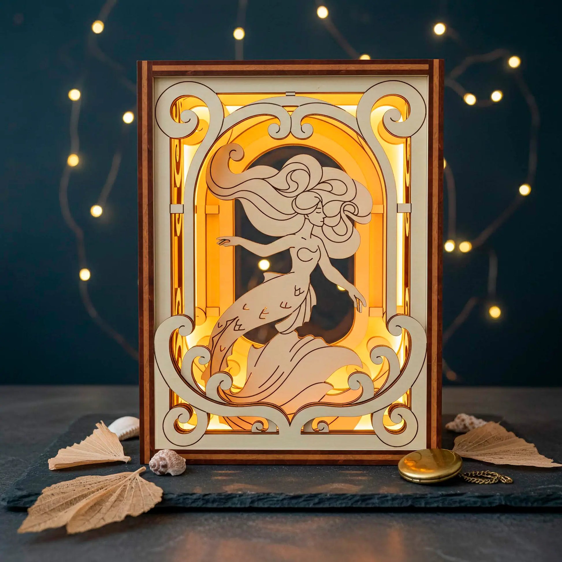 Laser cut wooden book nook with a mermaid design illuminated by a light source, surrounded by decorative elements on a dark background.