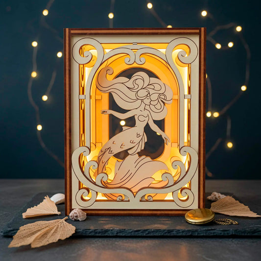Laser cut wooden book nook with a mermaid design illuminated by a light source, surrounded by decorative elements on a dark background.
