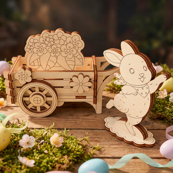 Wooden laser cut rabbit and cart decoration on a wooden surface with flowers and eggs.