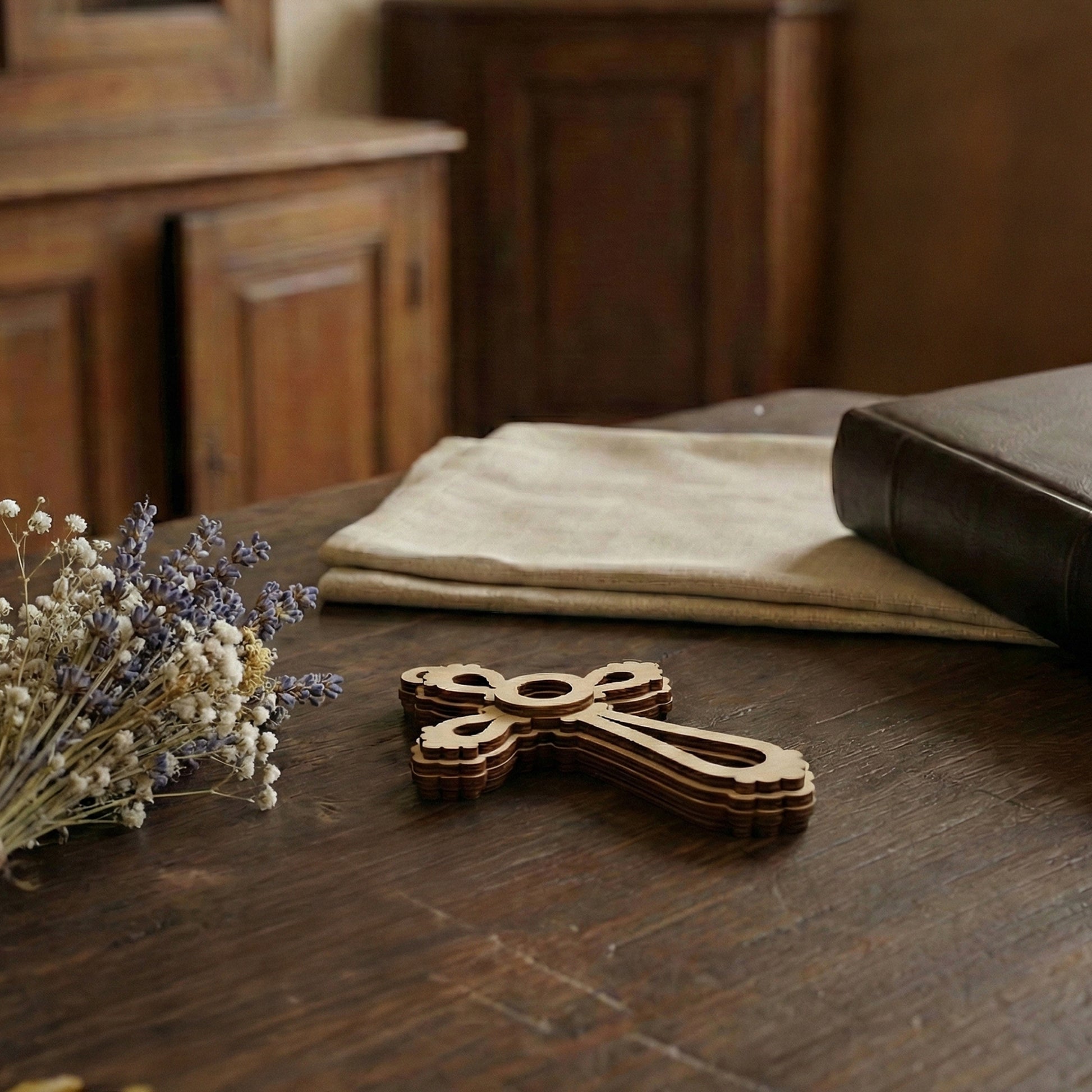 Wooden laser cut cross on a wooden table with flowers and a book in the background