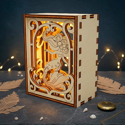 Decorative wooden book nook with laser cut mermaid on a dark surface with lights in the background
