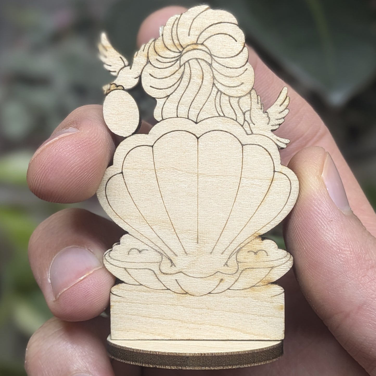 Back view of a laser cut plywood Aphrodite held in hand. Shows dark burnt wood edges, wavy hair, and natural grain texture