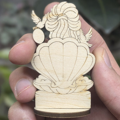 Back view of a laser cut plywood Aphrodite held in hand. Shows dark burnt wood edges, wavy hair, and natural grain texture