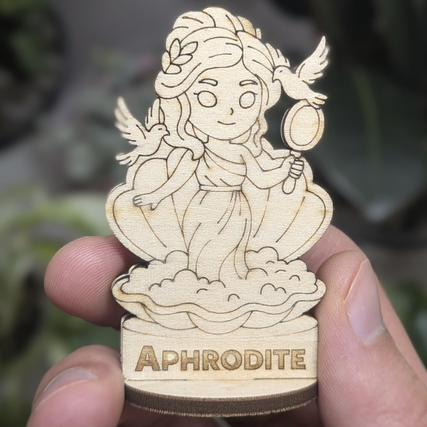 Hand holds a laser cut plywood Aphrodite for scale. Detailed front shows flowers in hair, dress, and heart at tiny scale