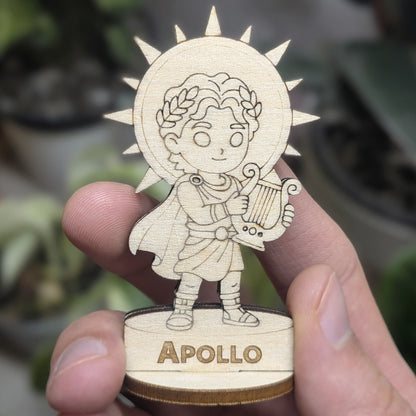 Hand holds a laser cut plywood Apollo for scale. Detailed front view shows the engraved lyre, laurel wreath, and wood robes
