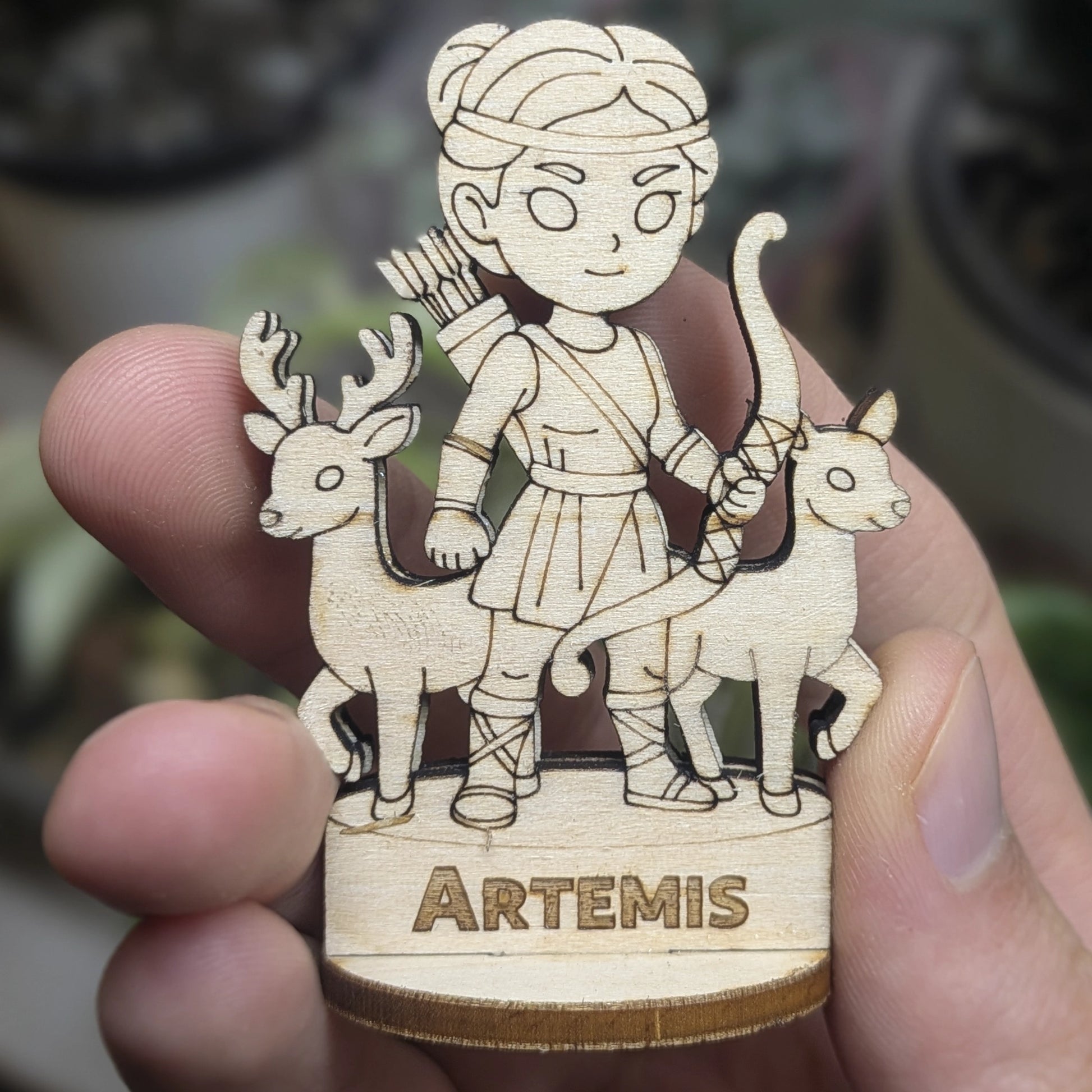 Hand holds a laser cut plywood Artemis for scale. Detailed front showing the hunting bow, tunic, and fine wood engraving