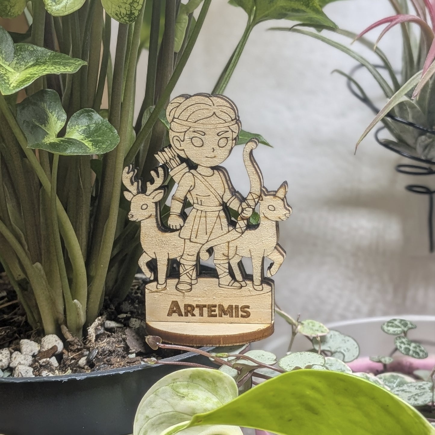 Laser cut plywood Artemis figurine sits in a plant pot. Features an engraved bow, hunting tunic, and short hair on a wood base