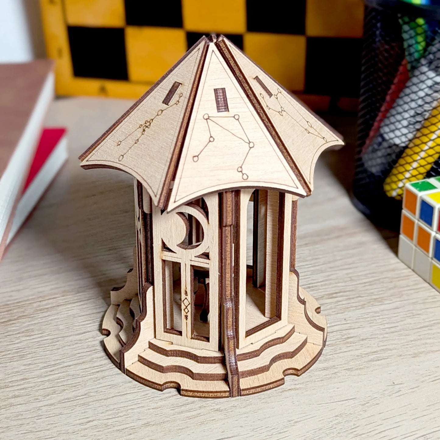 A crisp high angle shot of an assembled miniature astronomical gazebo model made from laser cut plywood on a dark counter.