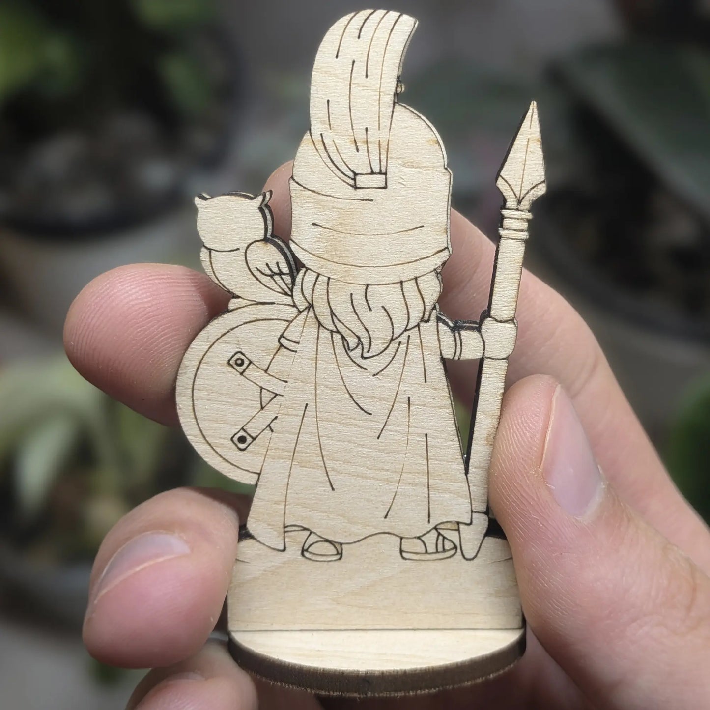 Back view of an Athena figurine made of laser cut plywood held in hand. Shows dark burnt edges and fine natural wood grain texture