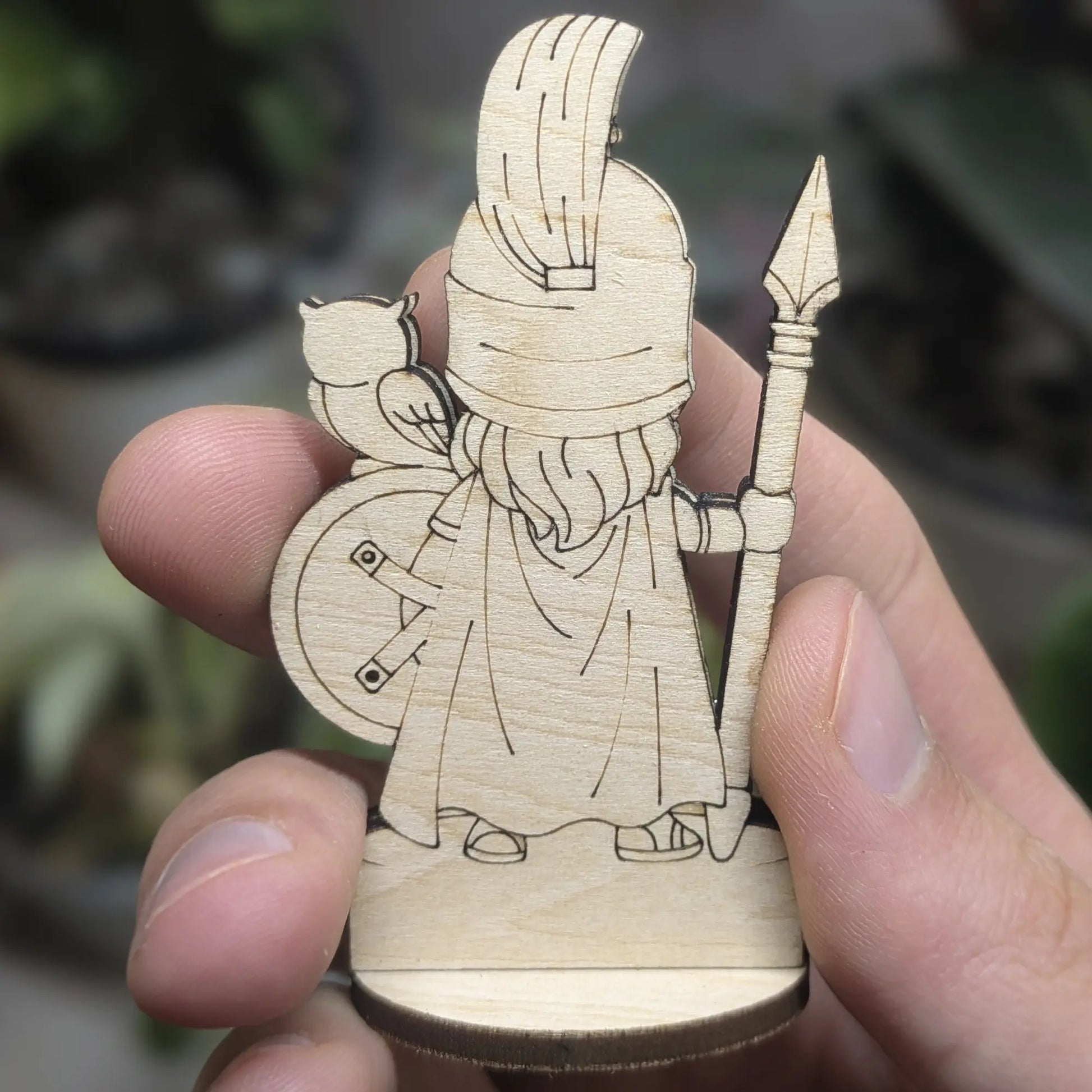 Back view of an Athena figurine made of laser cut plywood held in hand. Shows dark burnt edges and fine natural wood grain texture