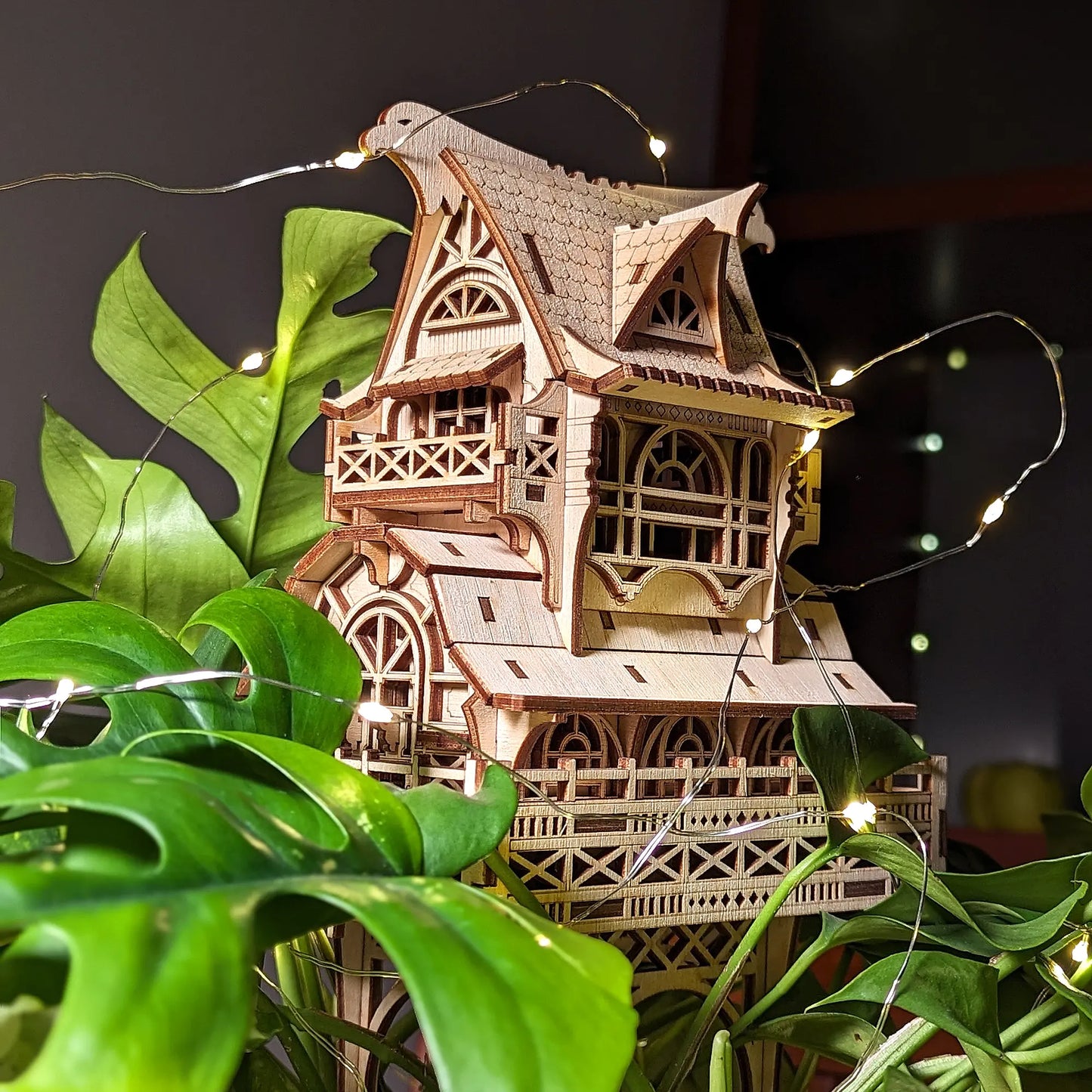 Full view of a laser cut plywood miniature wizard house decorated with small glowing lights inside a green plant.