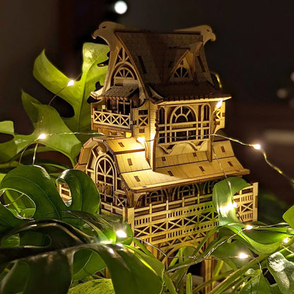 Low-light shot of a magical laser cut plywood dollhouse standing inside plant foliage with tiny sparkling lights.