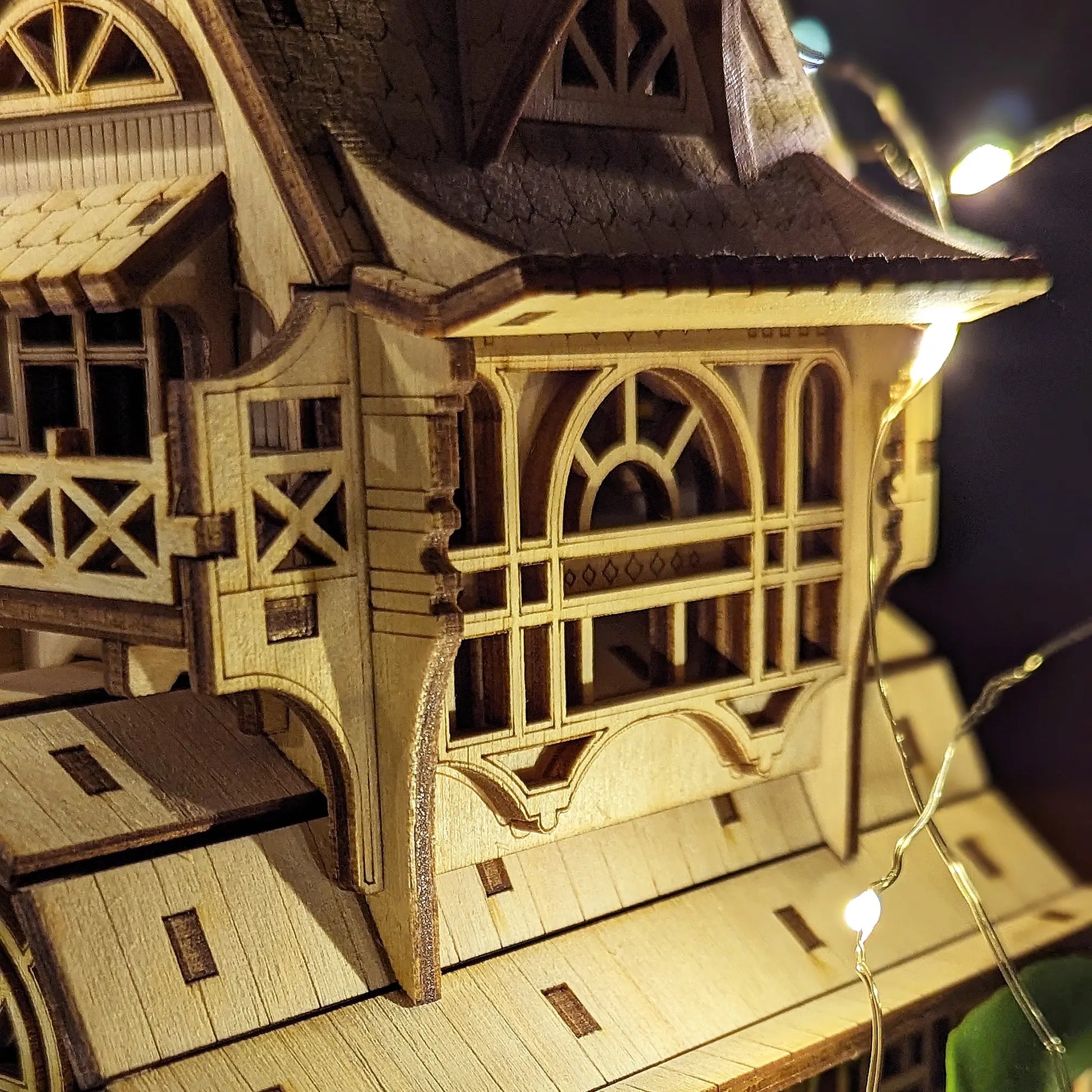 Macro shot of a laser cut plywood house facade showing intricate window frames, balconies, and burn mark accents.