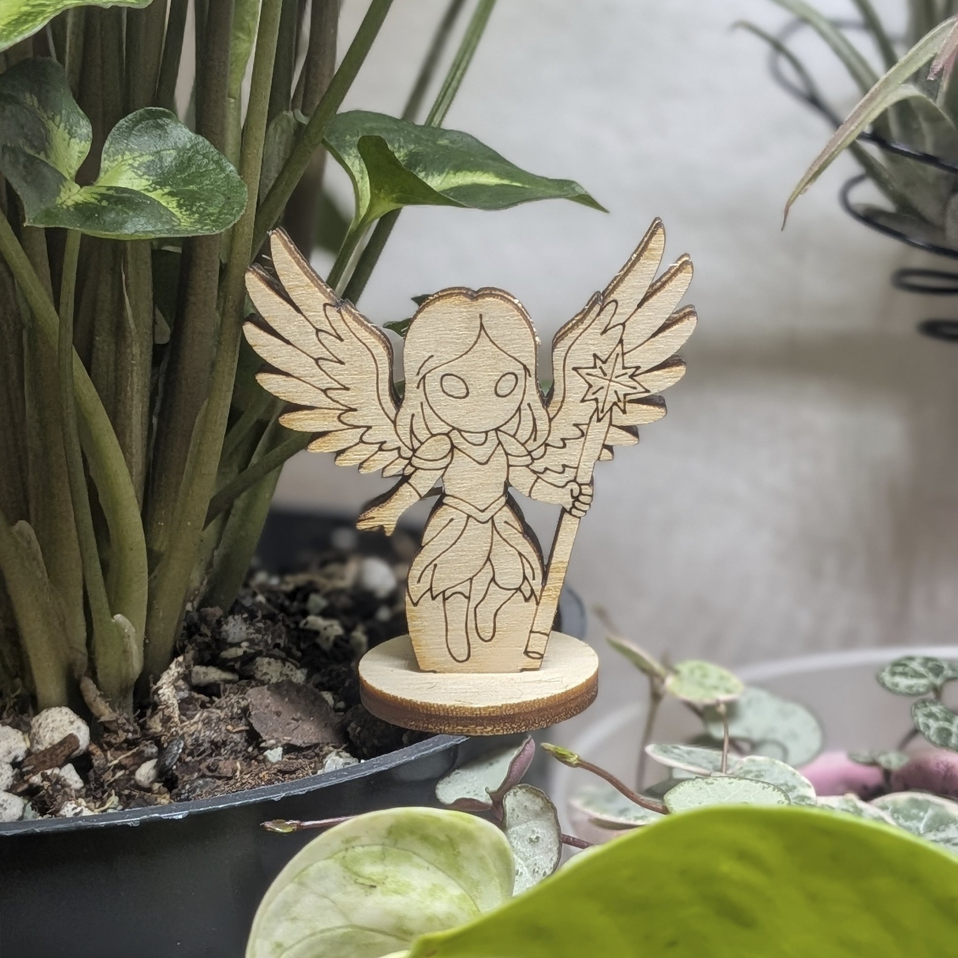 Laser cut plywood celestial angel figurine sits in a plant pot. Features large wings, a halo, and detailed praying hands