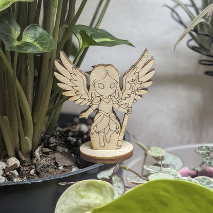 Laser cut plywood celestial angel figurine sits in a plant pot. Features large wings, a halo, and detailed praying hands