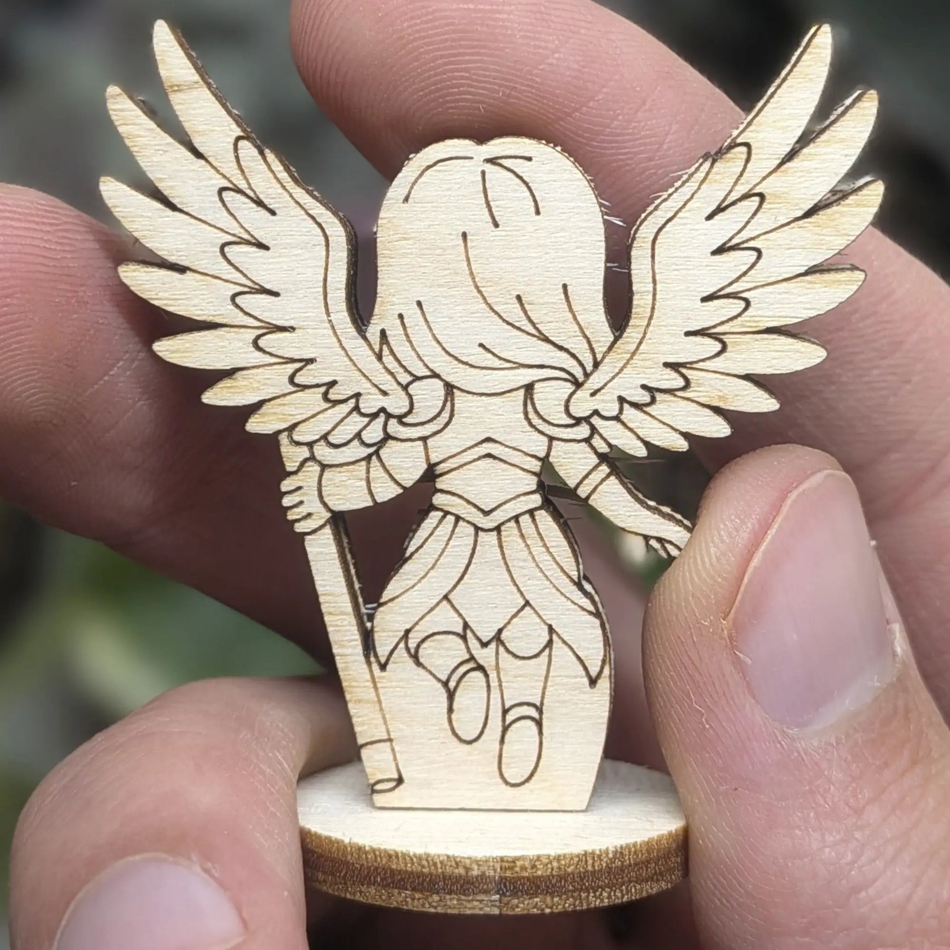 Back view of a laser cut plywood celestial angel held in hand. Highlights the dark burnt edges and natural wood grain textures