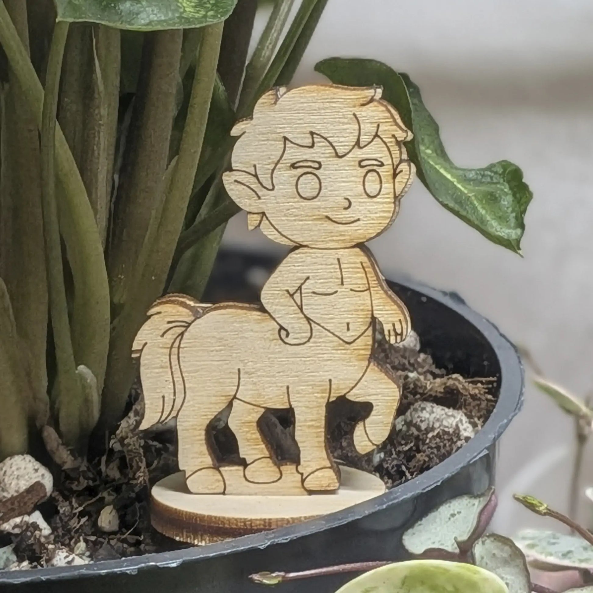Centaur miniature of laser cut plywood in a plant pot. Features a human torso, horse body, and detailed wood grain texture