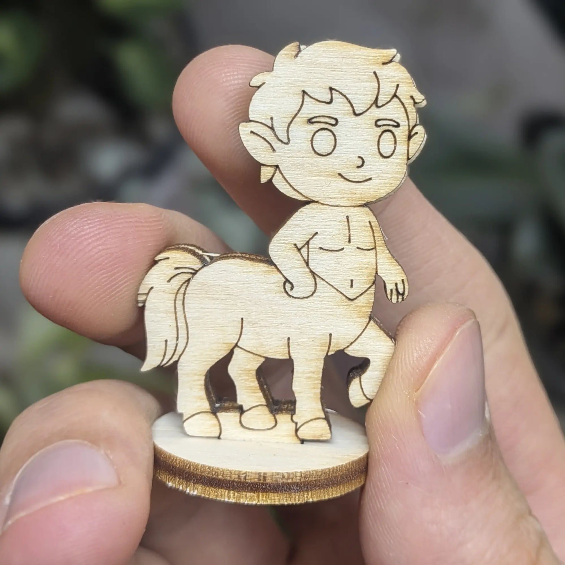 Hand holds a laser cut plywood centaur figure for scale. Showing engraved eyes, hair, and muscular horse legs on wood base