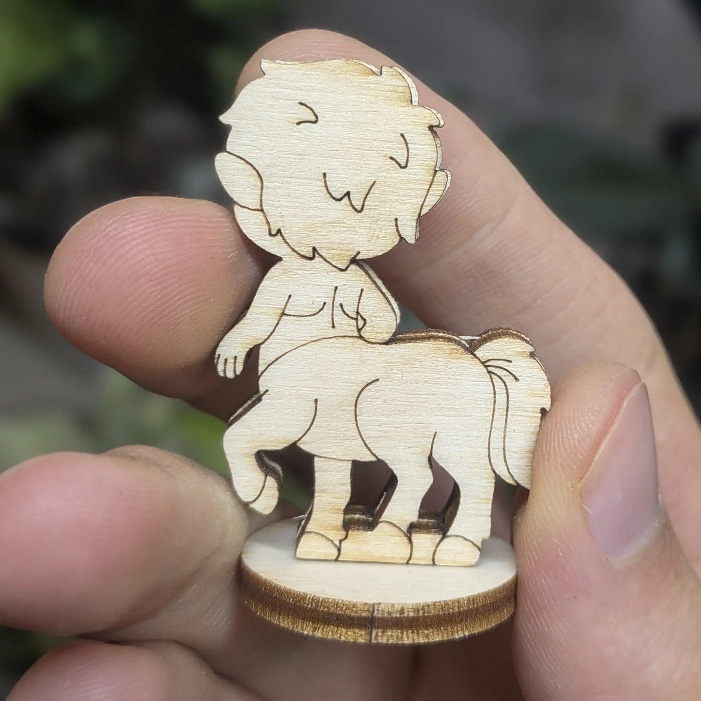 Back view of laser cut plywood centaur held in hand. Highlights the tail texture, dark burnt edges, and natural wood grain