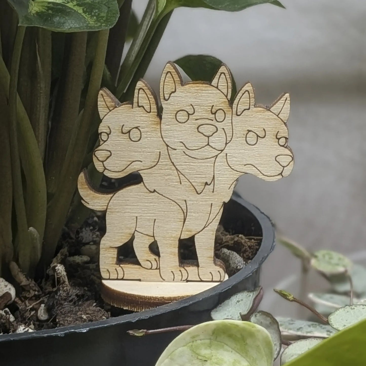 Back view of a laser cut plywood Cerberus held in hand, showing light wood grain, dark burnt edges, and smooth texture