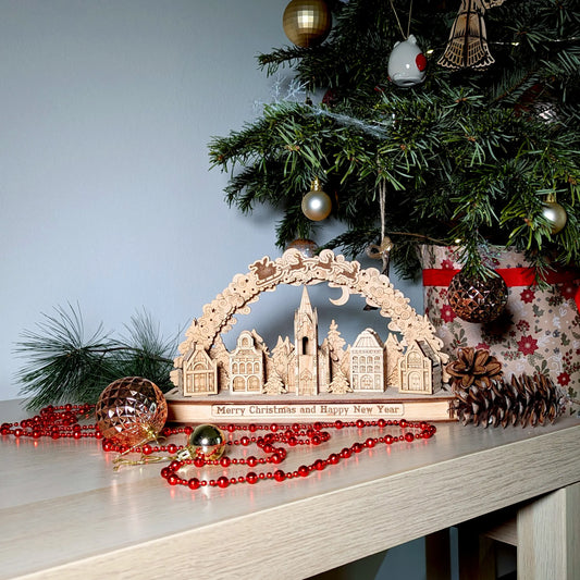 Staged wide photo of an assembled Christmas village arch display sitting underneath a holiday tree of laser cut plywood.