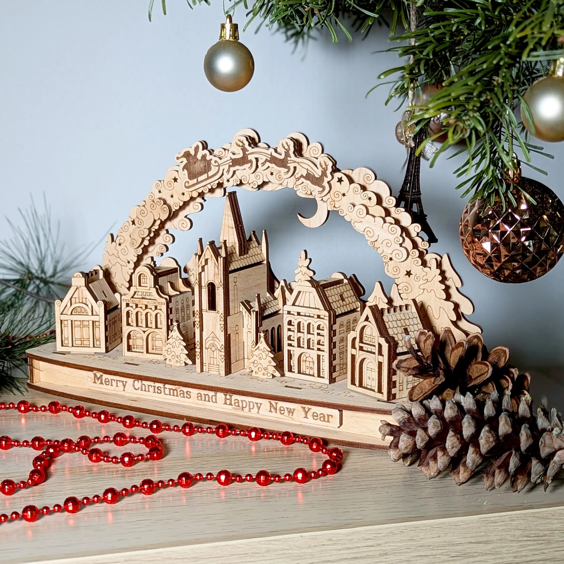 Staged eye-level photo of an assembled Christmas village skyline arch sitting near a pine cone from laser cut plywood.