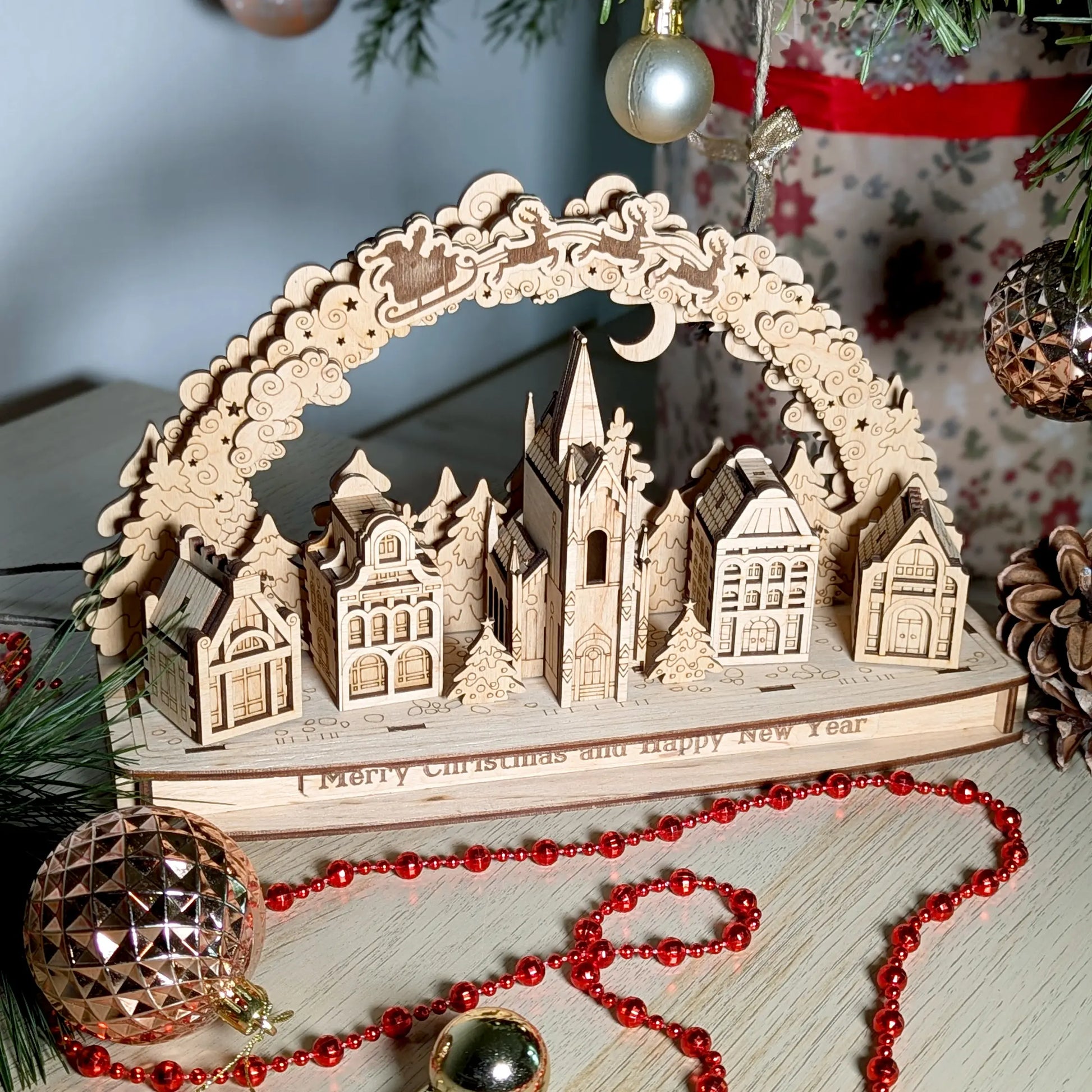 Staged high-angle photo of a completed Christmas town archway model decorated with festive red beads, laser cut plywood.