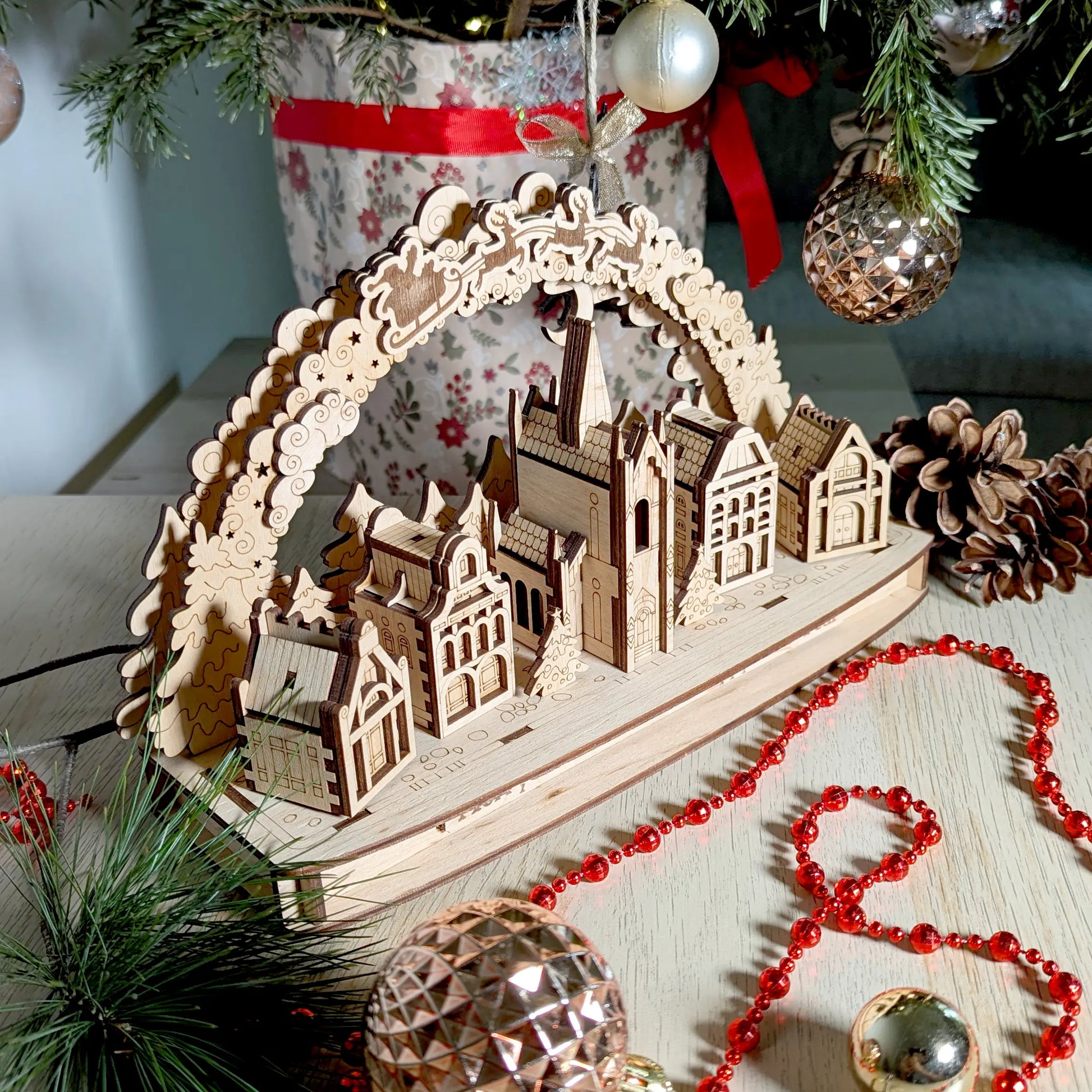 Assembled Christmas town arch display staged beautifully on a light wooden table with shiny red beads, laser cut plywood.
