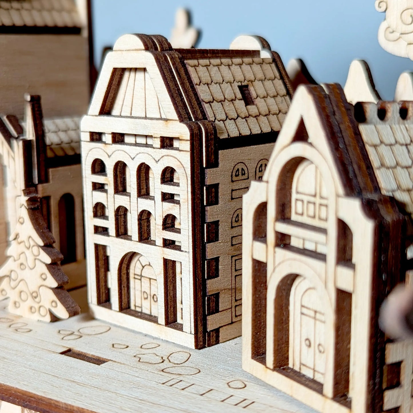 Detailed macro close-up photo focusing on two miniature holiday town house models featuring engraved laser cut plywood.