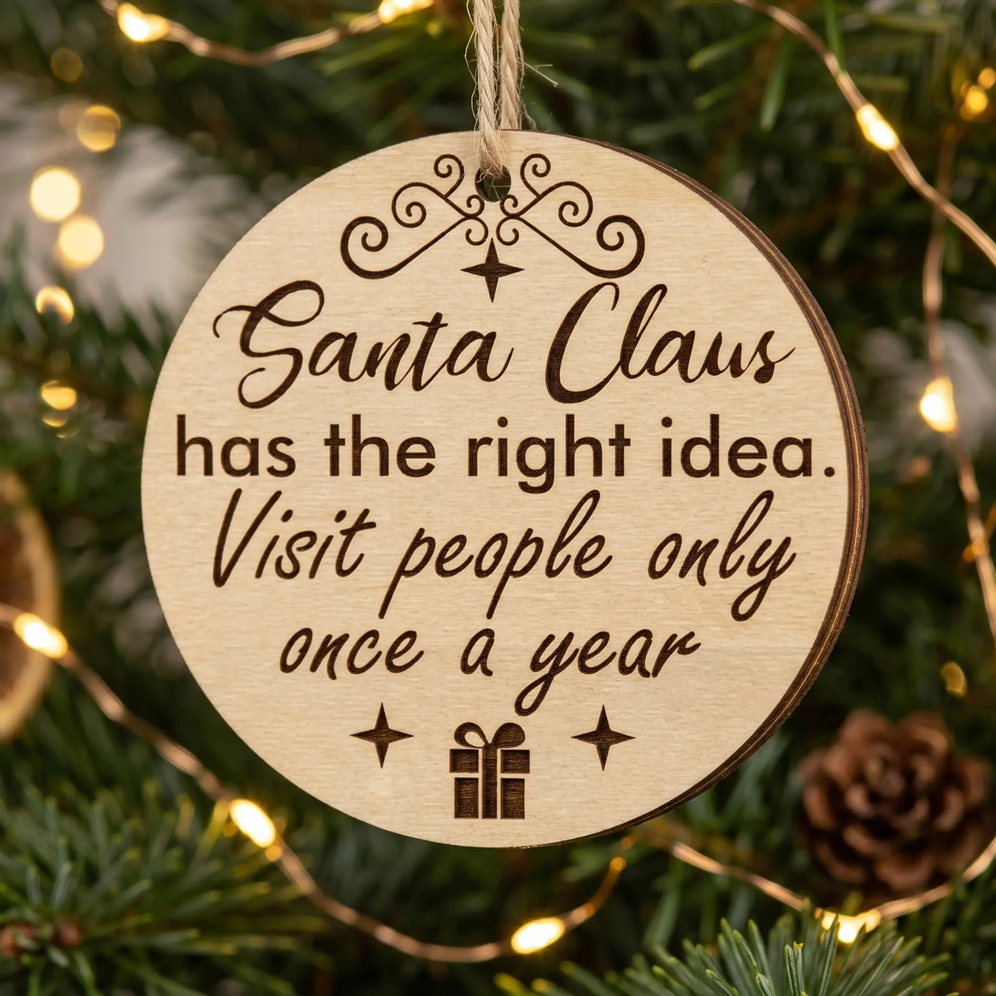 Laser cut plywood Christmas ornament with funny quote about Santa visiting once a year, hanging on a festive pine branch