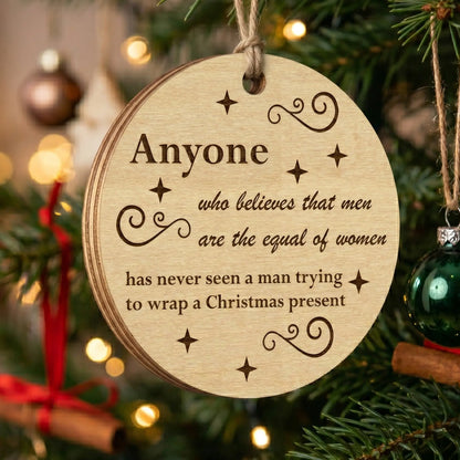 Round laser cut plywood Christmas ornament with a funny quote about gift wrapping, hanging on a branch with bokeh lights