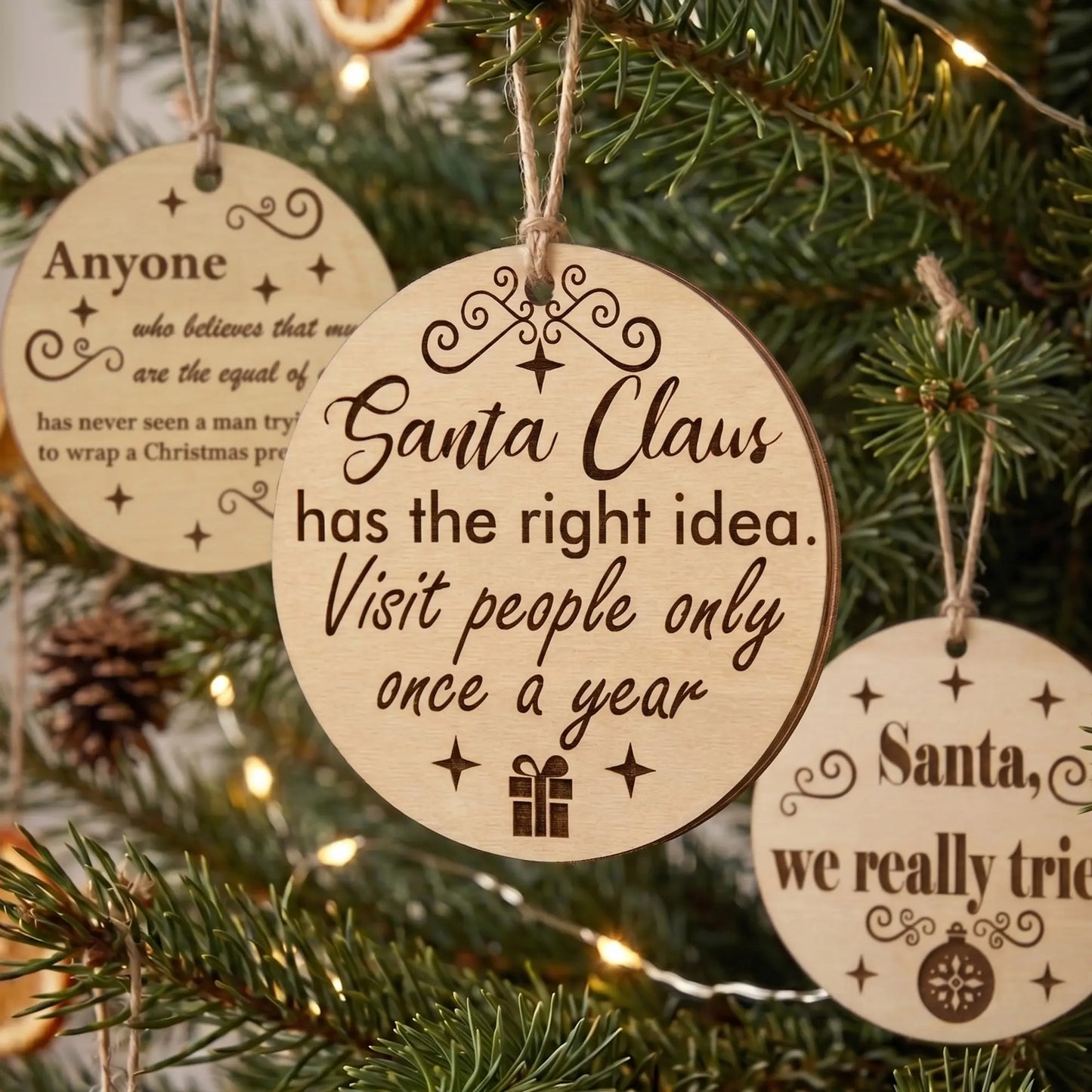 Group of round laser cut plywood Christmas ornaments with funny quotes hanging on a festive pine tree with twinkling lights.